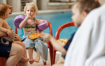 En familj sitter vid bassängkanten på Eriksdalsbadet i Stockholm och äter pommes frites och glass.
