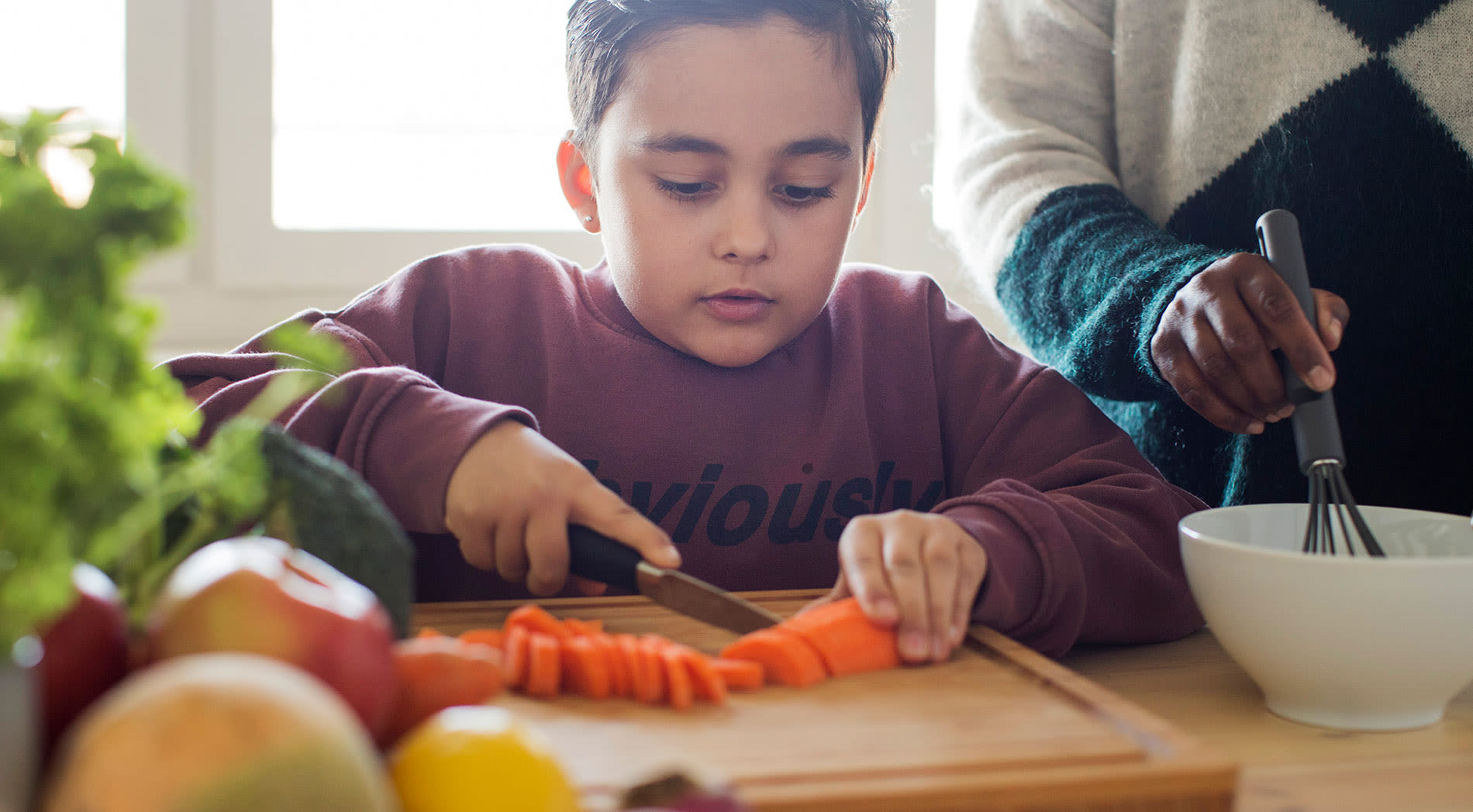 Kille sitter vid ett köksbord och skär morötter.