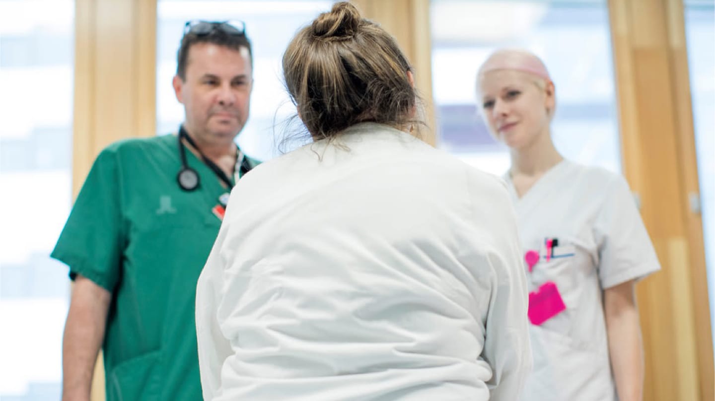 Patient sitter på en sjukhussäng. Framför står en doktor och en sjuksyster.