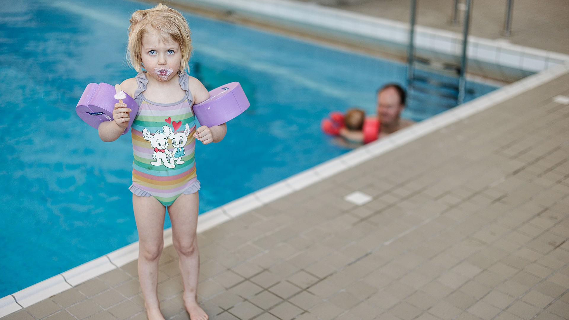 En flicka står emd en glass i handen vid en simbassäng.