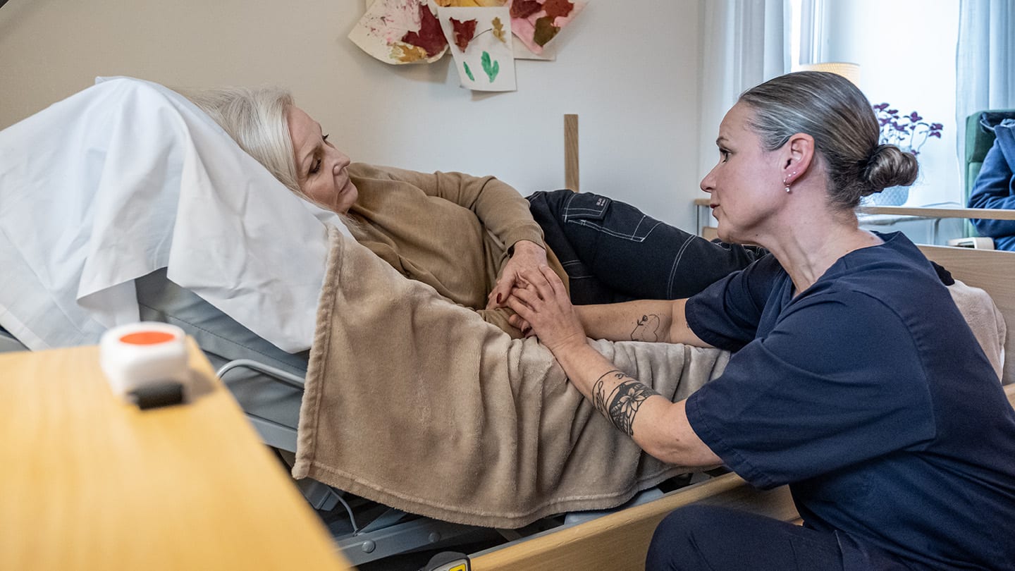 Sjuksköterska håller patient i handen i ett rum på palliativ avdelning