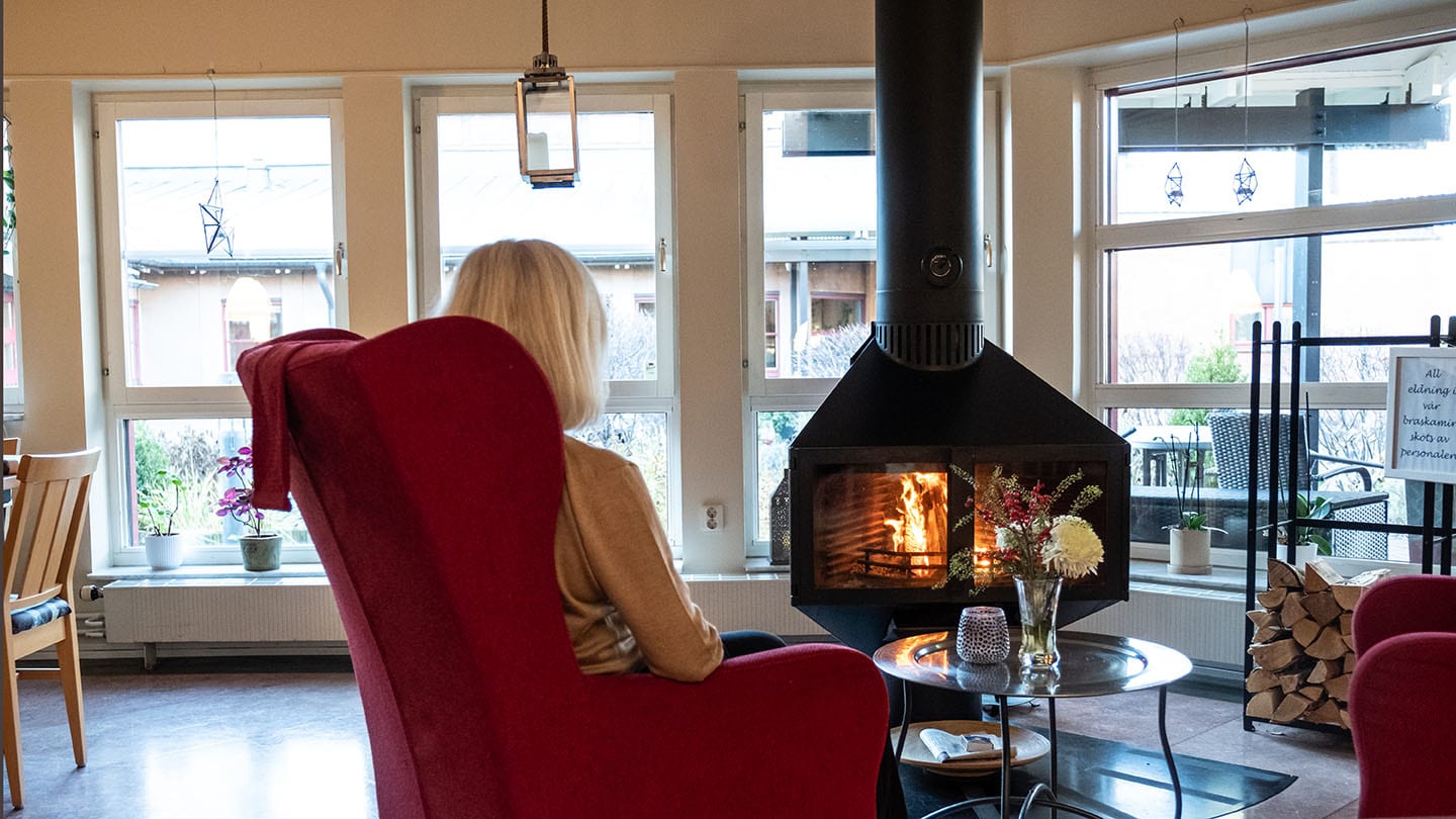 Kvinna sitter i fåtölj framför braskamin