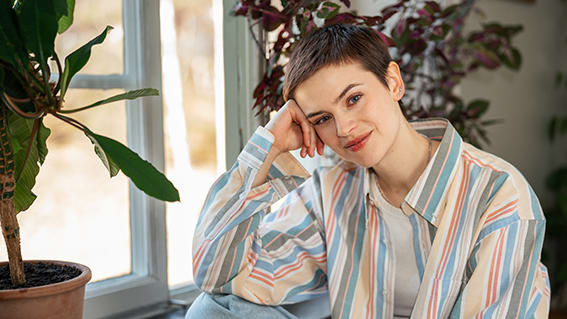 kvinna i kort brunt hår framför ett fönster med krukväxter