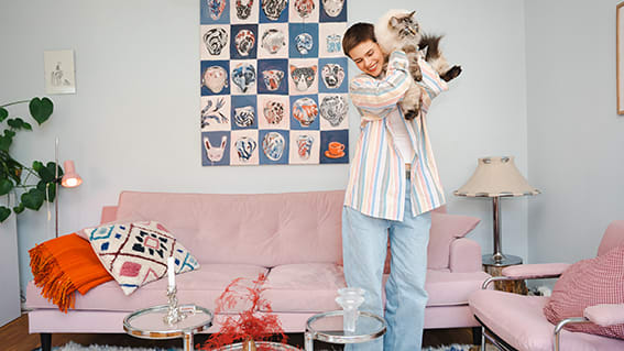 kvinna med katt på axeln framför en ljusrosa soffa