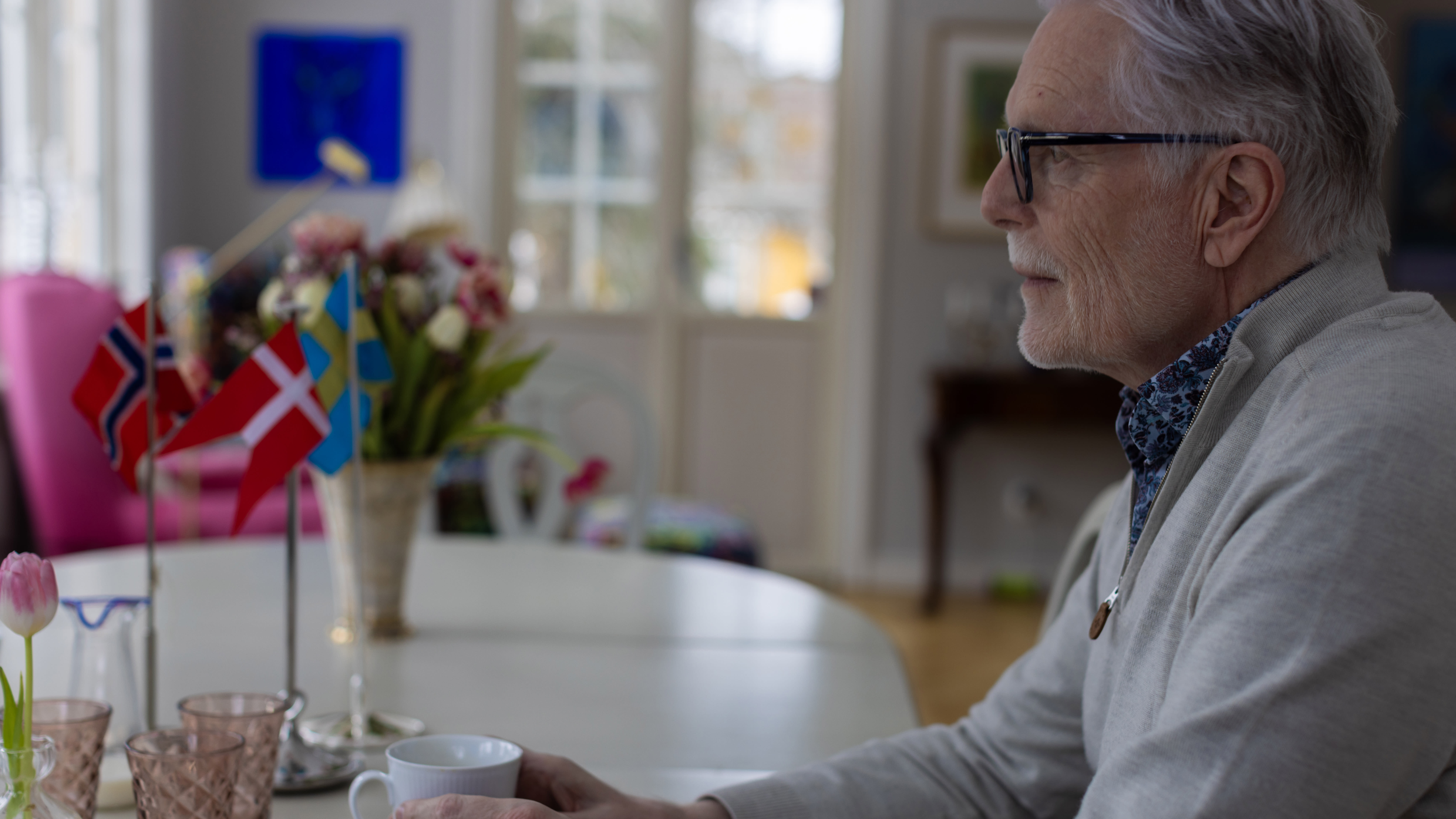 Ole sitter vid matsalsbordet med en kaffekopp i handen och blickar ut genom fönstret. Foto: Sanna Percivall.