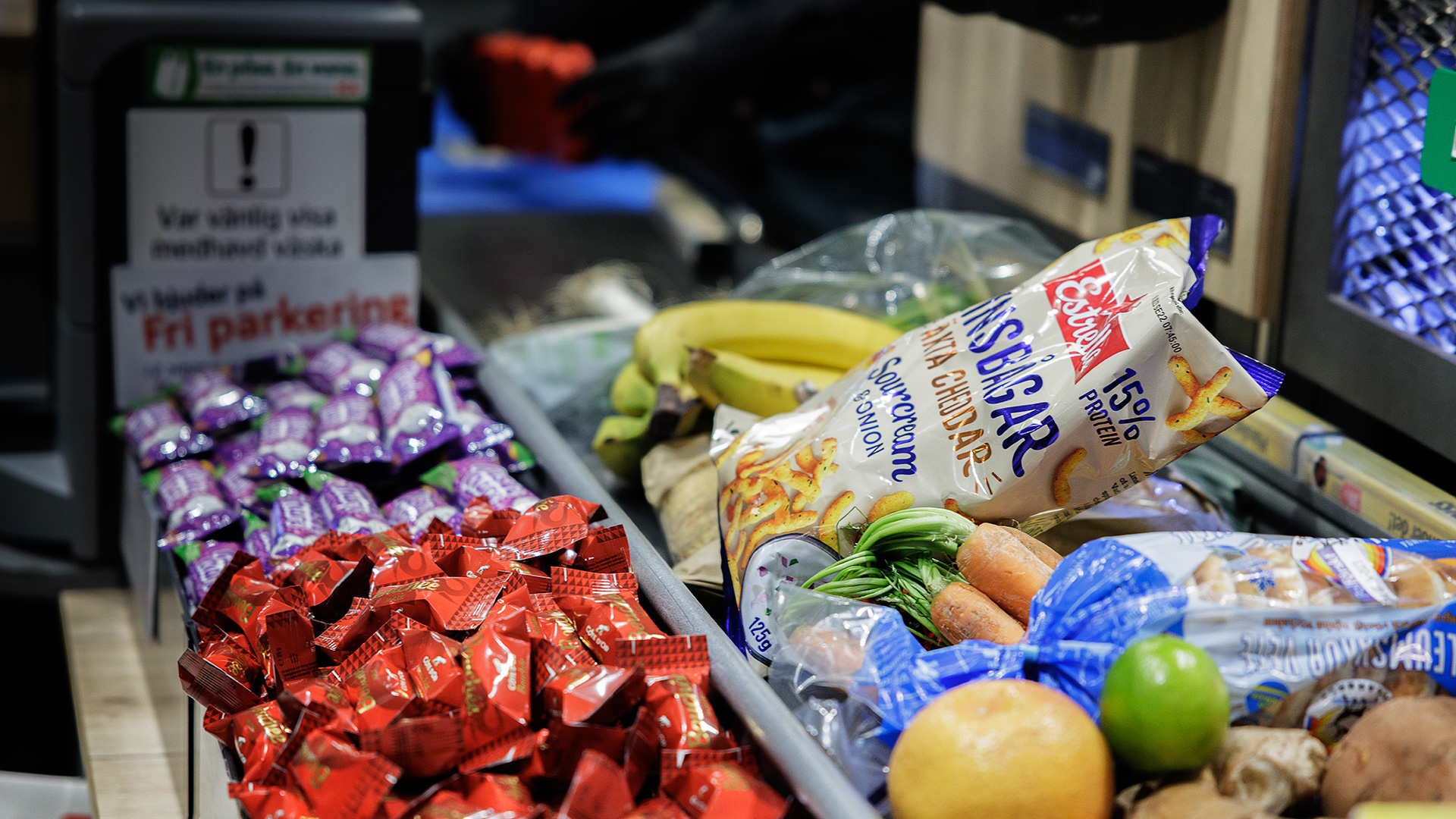 Ett varuband i kassan på en matbutik som är fullt med matvaror. Framför varubandet står ställ fyllda med godis och choklad.